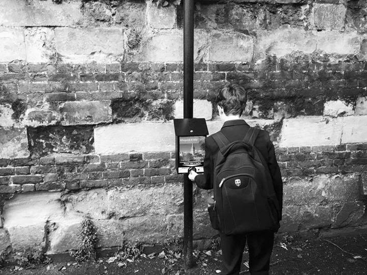 A man wearing a backpack standing in front of a brick wall