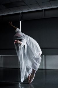 A woman dances in a dark room draped in a white cloth.