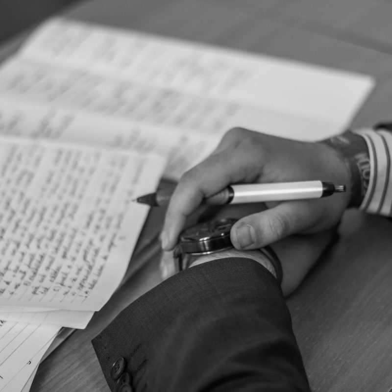Folded hands hold a pen near stacks of handwritten papers