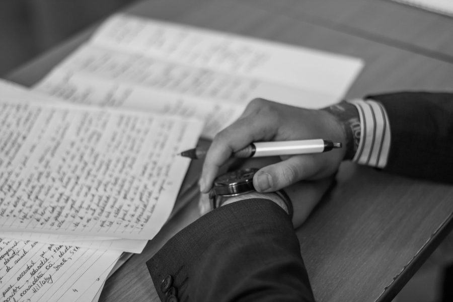 Folded hands hold a pen near stacks of handwritten papers