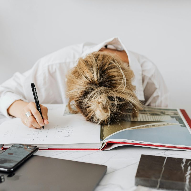 Woman writing in a notebook with her head down on the desk in frustration