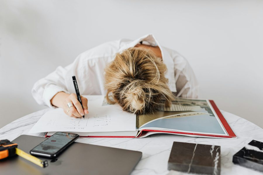 Woman writing in a notebook with her head down on the desk in frustration