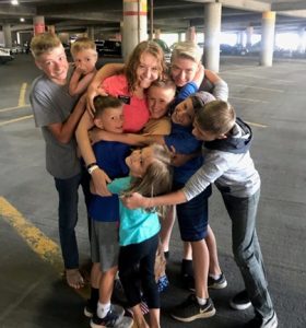 8 young siblings all hug their older sister, who wears a missionary name tag.
